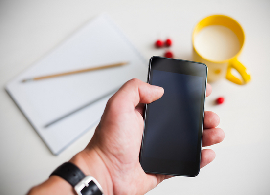 Man using smartphone, close-up, cup of milk and planning book on